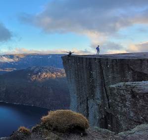 A person standing on a cliff edge with Preikestolen in the background AI-generated content may be incorrect.